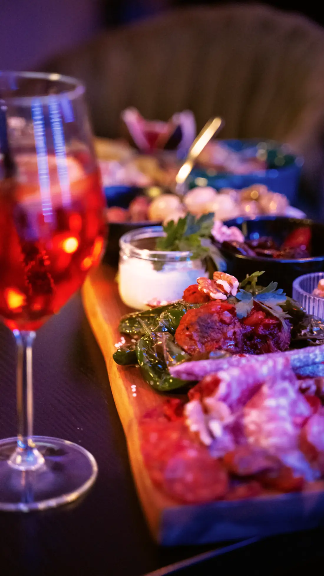 Weinglas vor einer Tapasplatte im farbigen Licht der Bar