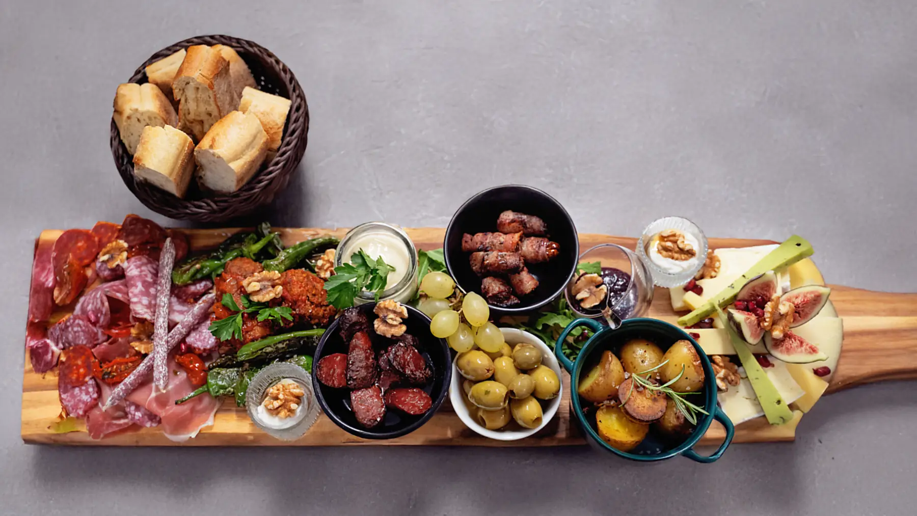 Große Tapasplatte auf einem Holzbrett mit Schinken, Oliven, Nüssen und Dips